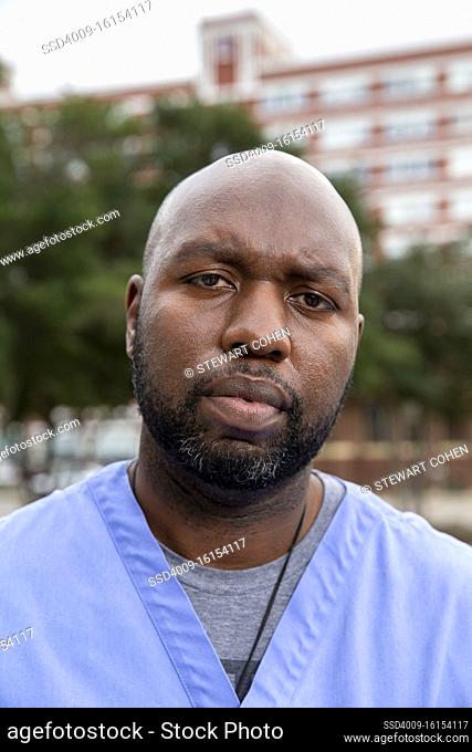 Portrait of middle aged man with beard and a bald head wearing scrubs standing outside looking at camera