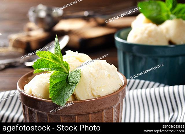 Vanilla icecream balls in clay bowls on wooden kitchen table with ice cream scoop aside