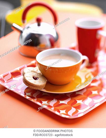 Orange cup and saucer on tray with biscuit and stainless steel kettle