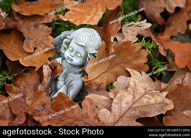 01 November 2022, Bavaria, Kempten: A figure of an angel lies on a grave among autumn leaves at the Central Cemetery. Photo: Karl-Josef Hildenbrand/dpa