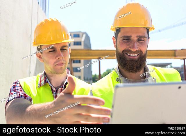 Two young workers watching a video with useful information or communicating online through a tablet PC during break on the construction site