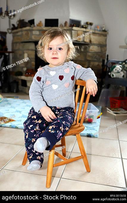 kleines Mädchen sitzt im Wohnzimmer auf einem Kinderstuhl aus Holz - little girl sitting on a wooden child chair in living room