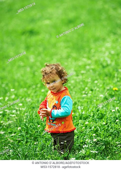 A one year old baby girl playing in a green meadow