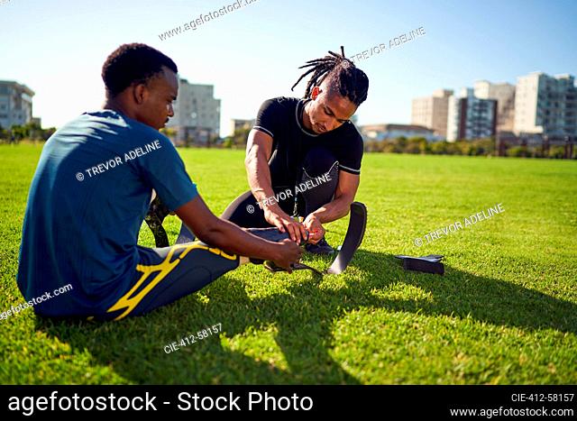 Coach helping young male amputee athlete with running blade prosthetic