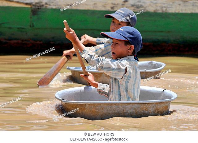 Cambodia, Siem Reap, Young boys using a bowl to float around the boats in the lake at Floating Village of Chong Kneas, Tonle Sap