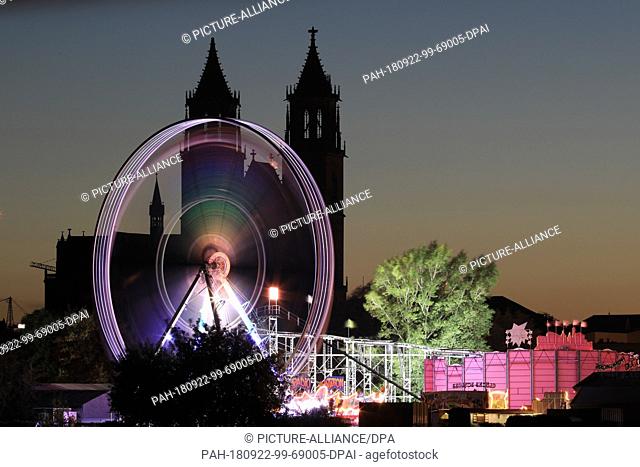 21 September 2018, Saxony-Anhalt, Magdeburg: A Ferris wheel shines in front of the silhouette of the Cathedral ""Saint Catherine and Saint Mauritius"" in...