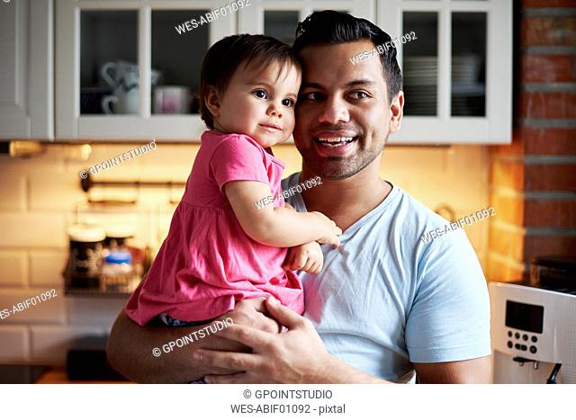 Smiling father holding baby girl in kitchen at home