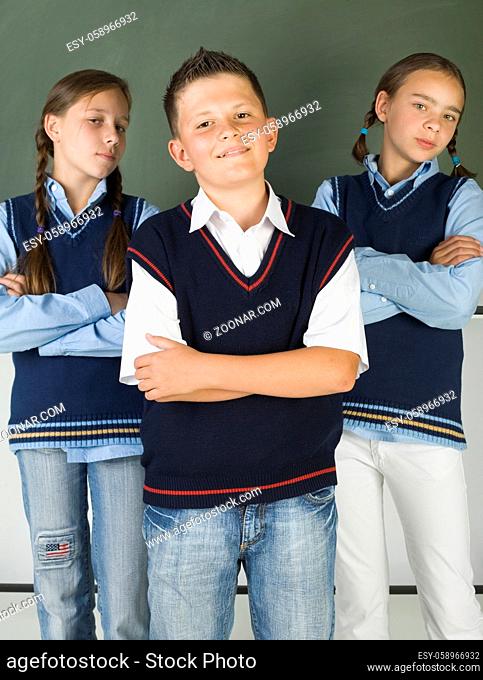 Two, young girls and one boy standing proudly in front of blackboard. Smiling and looking at camera. Front view
