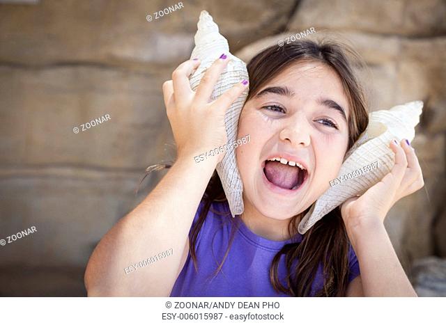 Young Girl Playing with Large Sea Shells Against Her Ears