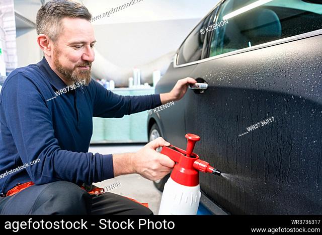 Man preparing car for putting advertisement sticker on it spraying water on the door