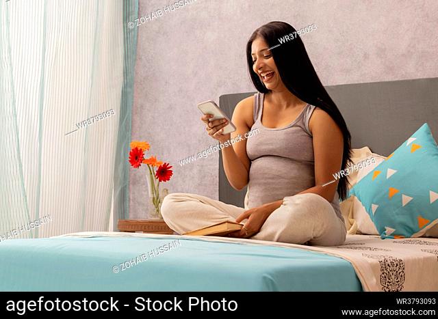 Pregnant woman using mobile phone while sitting on bed