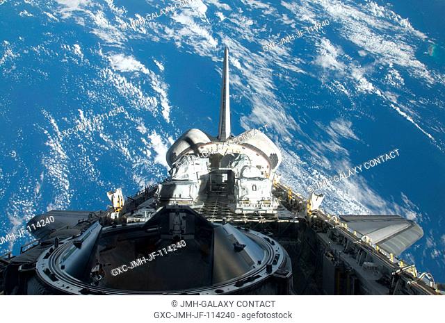 Backdropped by a blue and white part of Earth, a partial view of Space Shuttle Atlantis' payload bay, vertical stabilizer