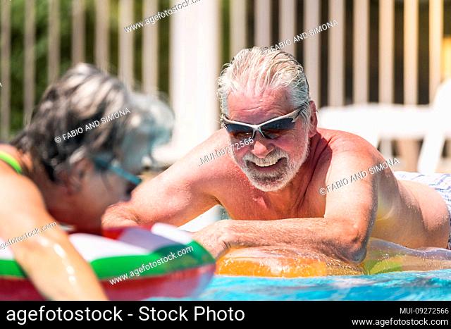 Cheerful happy smiling people senior man enjoying the summer swimming pool in couple retired nice lifestyle - white hair and summer holiday vacation or relax...
