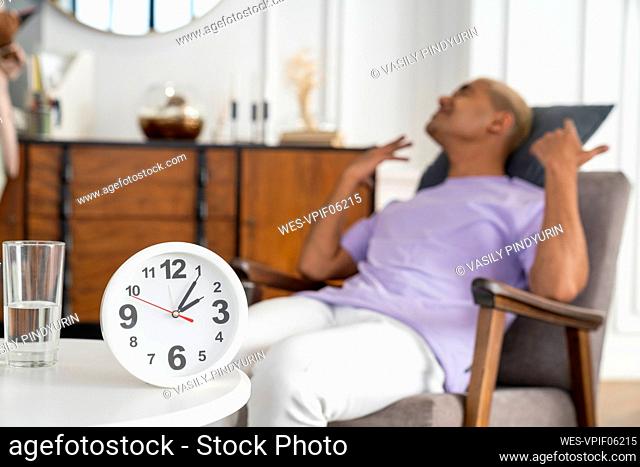 Clock on table with stressed patient sitting in armchair