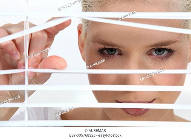 a blonde woman looks through blinds