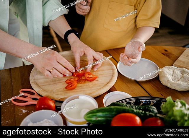 Mother helping son with tomato slices at home