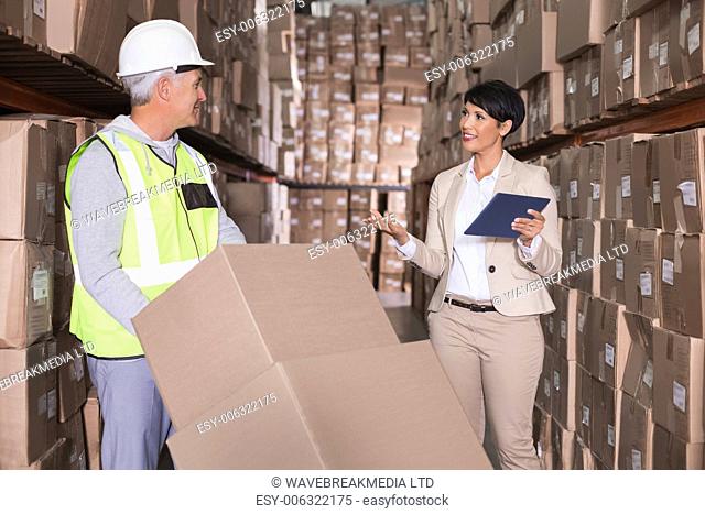 Warehouse worker moving boxes on trolley talking to manager in a large warehouse