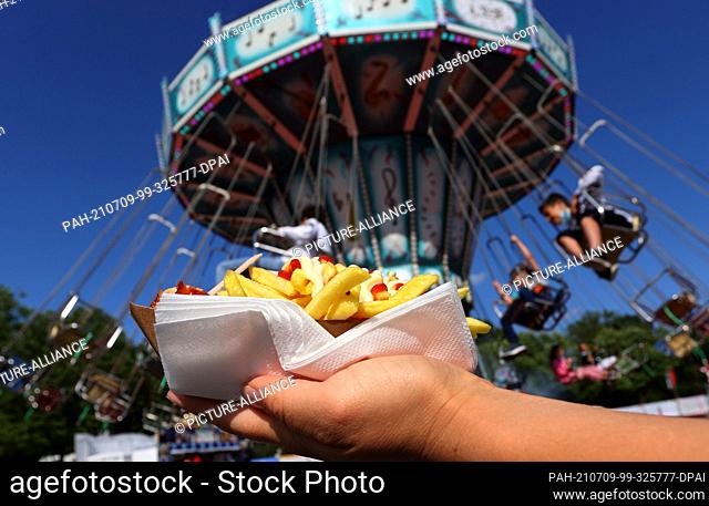 09 July 2021, Baden-Wuerttemberg, Weingarten: A visitor to the Welfenfest holds French fries in front of the chain carousel