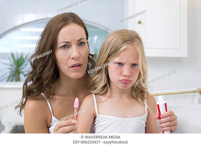 Mother and displeased daughter with toothbrush and toothpaste