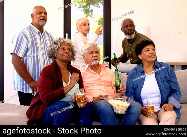 Multiracial senior friends with beer and popcorn watching soccer match in nursing home