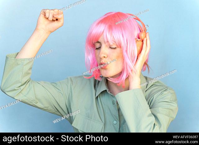 Portrait of young woman wearing pink wig listening to music with headphones