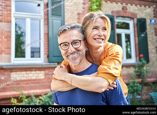Happy woman embracing man from behind in front of house