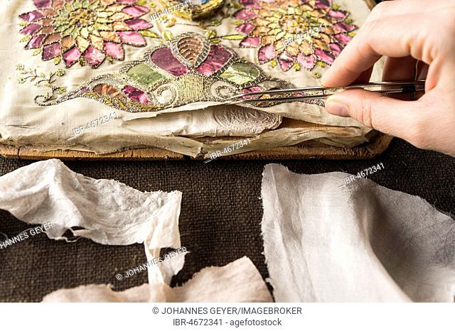 Restoration studio, restorer, hand checks artistically embroidered silk cloth torn open with tweezers, Munich, Bavaria, Germany