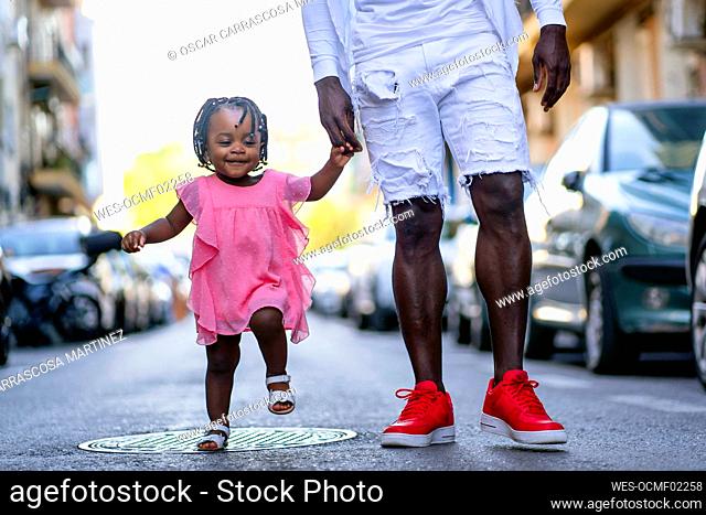 Girl holding hand of father while walking on road