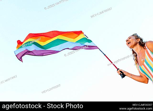 Mature woman swaying gay pride flag against clear sky