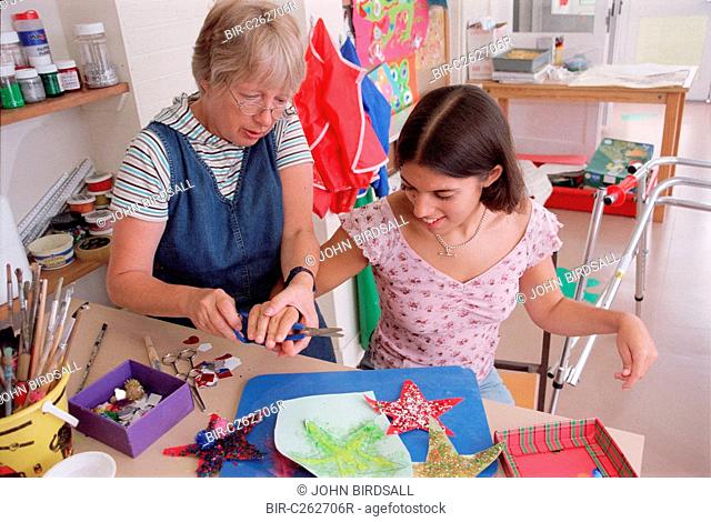 Carer assisting teenage girl to use self opening scissors in residential respite care home