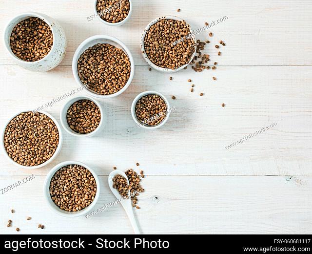 Hemp seeds in small white bowls and spoon on white wooden table. Set of small bowls with raw organic unrefined hemp seed. Superfood and vegan concept