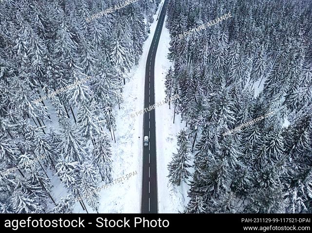 29 November 2023, Hesse, Niederreifenberg: A car drives along snow-covered trees on a country road in the Taunus. (Aerial shot with a drone)