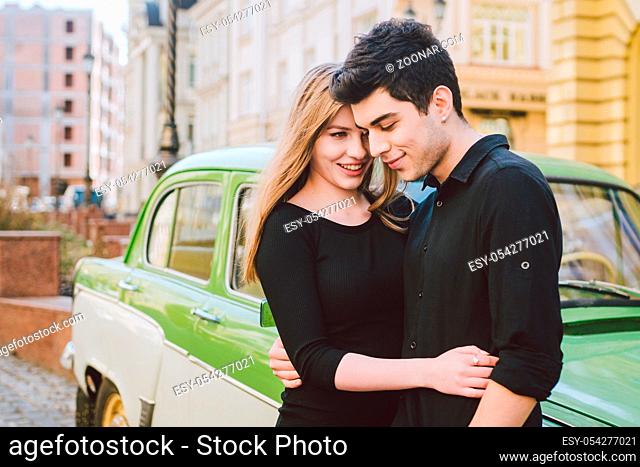 Young multiracial couple, male and female lovers heterosexual people students. Beautiful models posing standing near a retro car in the city