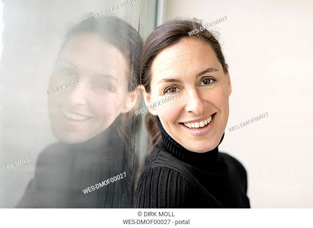 Reflection and portrait of smiling businesswoman wearing black turtleneck pullover