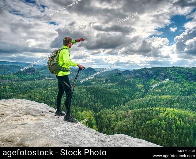 Athlete ginger hair man tourist hiking mountain trail, walking on sandstone rocky hill, wearing backpack and sunglasses, using trekking sticks