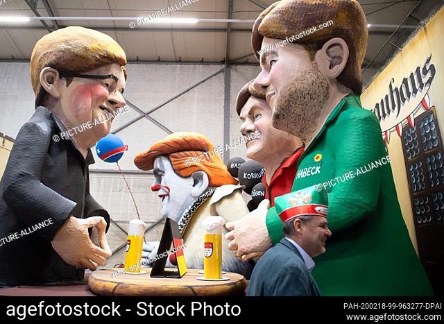 18 February 2020, North Rhine-Westphalia, Cologne: A visitor wearing a fool's cap walks past a carnival float with the cardboard figures of Armin Laschet (CDU