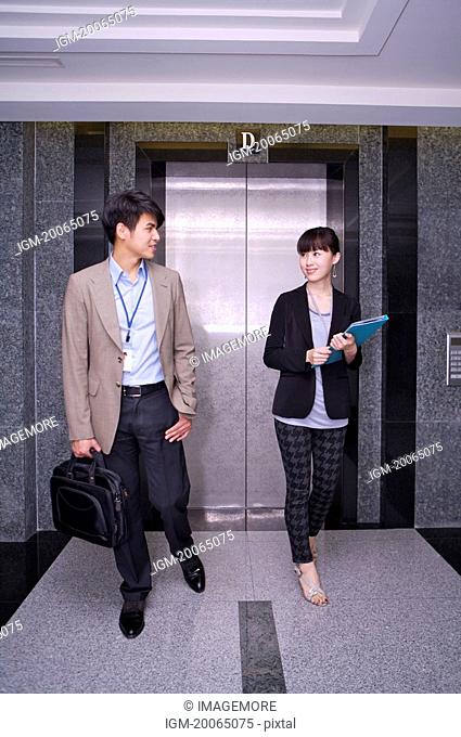 Young man and woman walking before elevator and talking together
