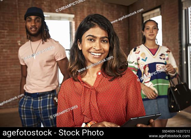 Group of friends in empty loft space, socially distanced group photo, focus on woman in foreground holding tablet