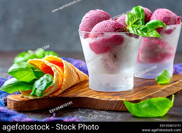 Artisanal blueberry ice cream in glasses with green basil on a wooden serving board on a dark textured background. Selective focus