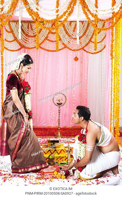 Bridegroom putting a toe ring onto the bride's toe during South Indian wedding ceremony
