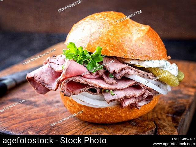 Traditional sliced cold cuts roast beef sandwich with onion, gherkin and remoulade offered as closeup on an old wooden board
