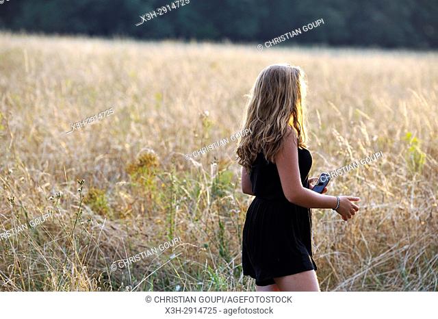 young girl listening music with her portable media player in a field at sunset, France, Europe