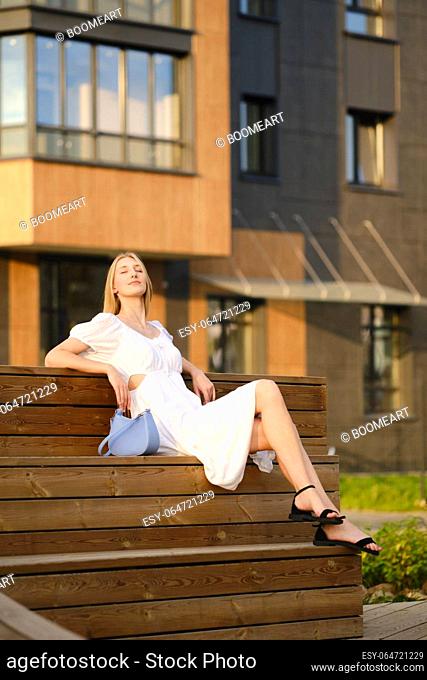 Cheerful woman sitting on bench and enjoying warm evening sun