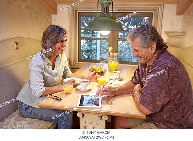 Senior couple enjoying breakfast and using digital tablet