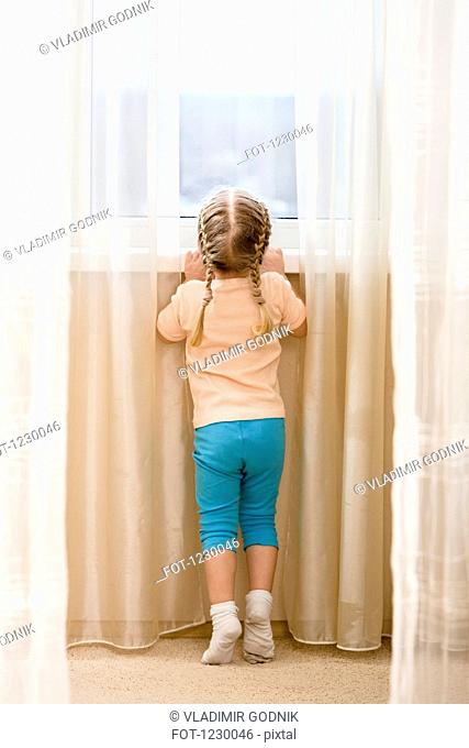 Little girl on her tiptoes trying to see out window