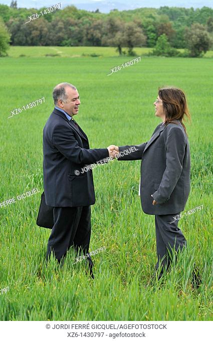 businesswoman and businessman shaking hands in green nature