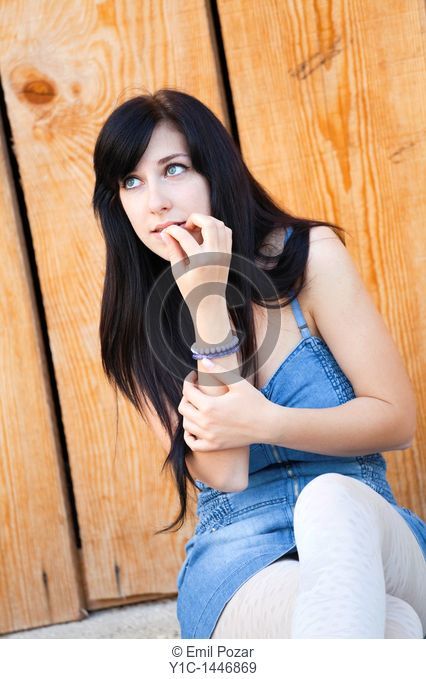 Attractive young woman is sitting and thinking, biting fingernail