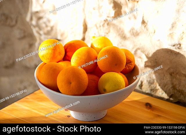 26 March 2023, Portugal, Tomar: Oranges and lemons lie in a bowl that stands on a sideboard in front of a stone wall. Photo: Viola Lopes/dpa