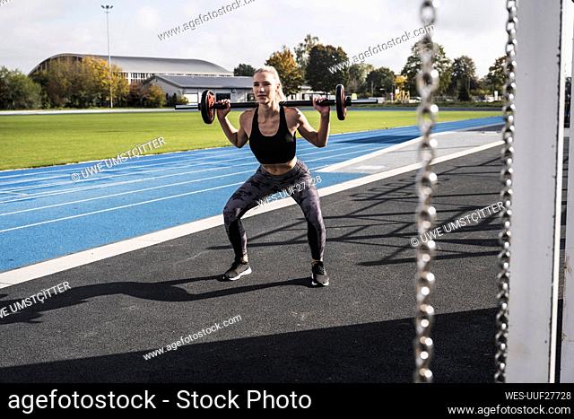 Young sportswoman exercising with barbell by running track