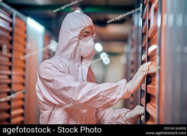 Worker in a respirator mask and hazmat suit closing the door latch of the shipping container
